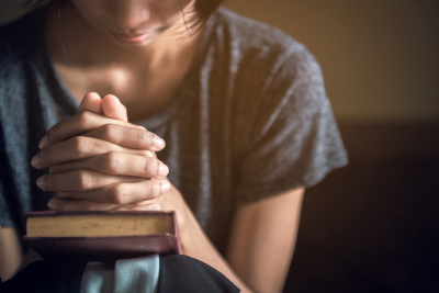 Soft focus on a hand of woman while praying for christian religion with blurred of her body background 